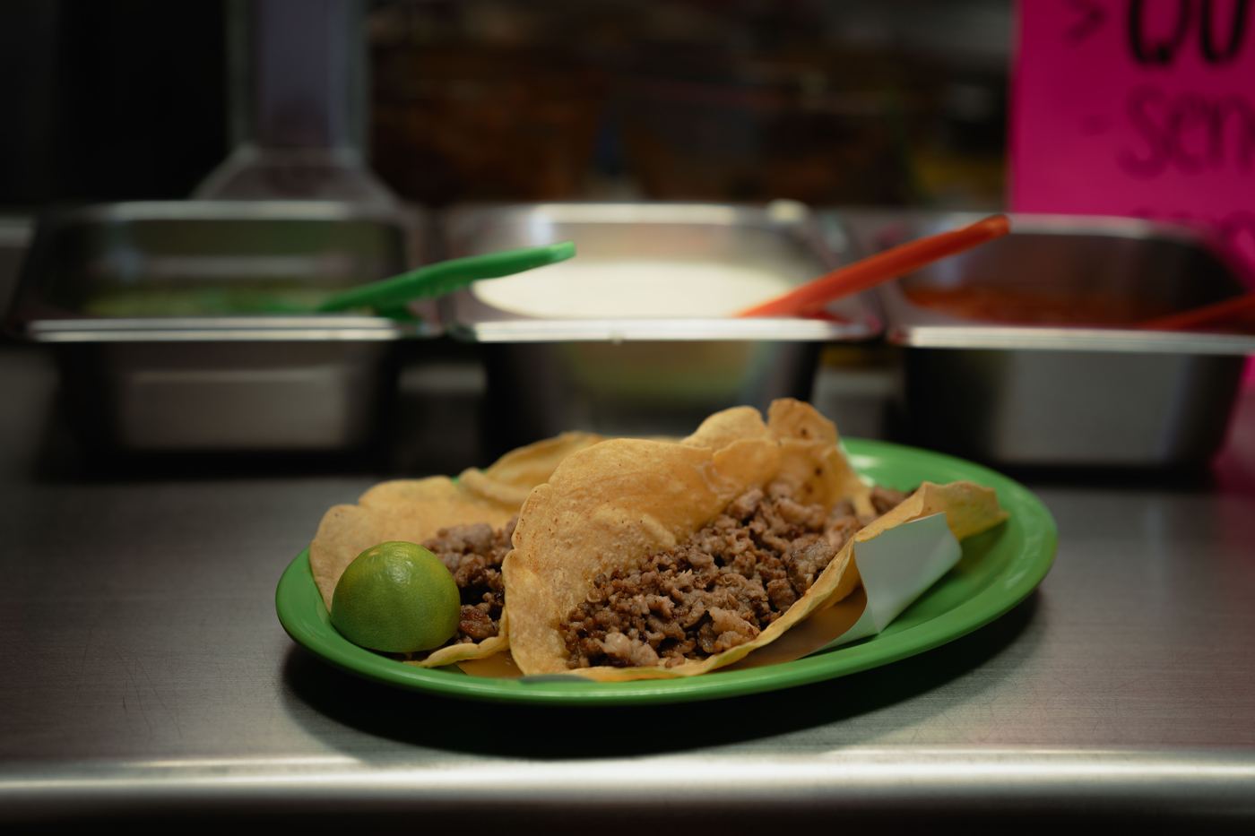 Tacos and a lime on a green plate, photographed at a food counter
